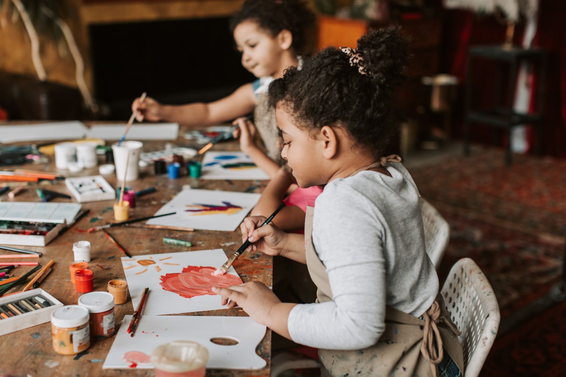 Two young children painting with brushes and colors in an indoor art workshop.