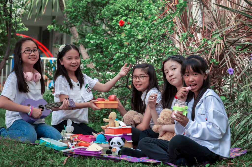 Group of children having a picnic outdoors with toys and snacks, enjoying friendship and nature.